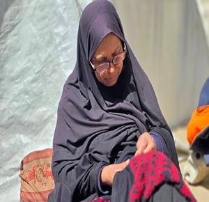  المواطنه سهيلة عيسى، تعود إلى تطريز الفساتين داخل خيمة نزوح في خان يونس جنوب قطاع غزة، بعد أن دمر الجيش الإسرائيلي منزلها، وتمارس سهيلة هذه الحرفة منذ 47 عاماً