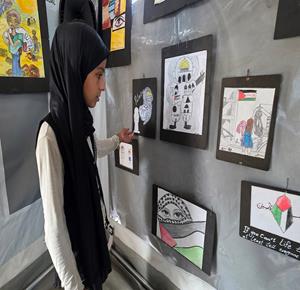 أطفال يعرضون أعمالهم الفنية خلال معرض «ألم وأمل.. واقع وخيال»، ضمن أنشطة المخيم الصيفي لتلاميذ مدرسة الأرض الطيبة في مواصي خان يونس جنوب قطاع غزة